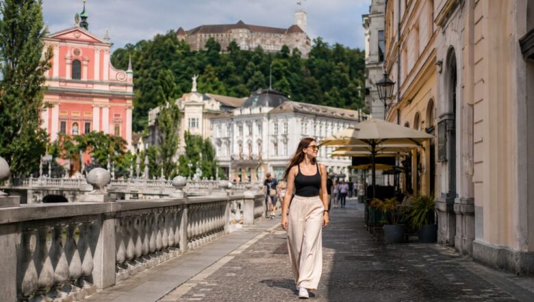 Solo female traveler walking along the riverside promenade in Ljubljana, with historic buildings and Ljubljana Castle in the background