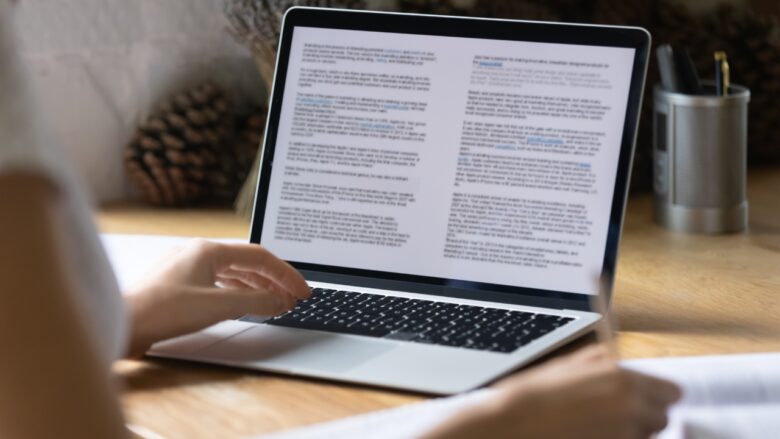 A student reviews an essay draft on a laptop beside paper notes