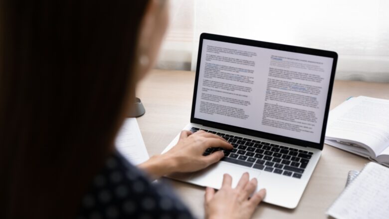 A student edits an essay draft on a laptop beside open notes