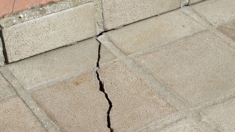 Cracked patio tiles beside a home show exterior surface damage