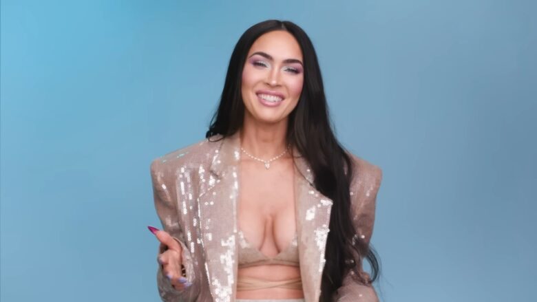 Megan Fox in a sequined blazer and beige top poses against a blue backdrop