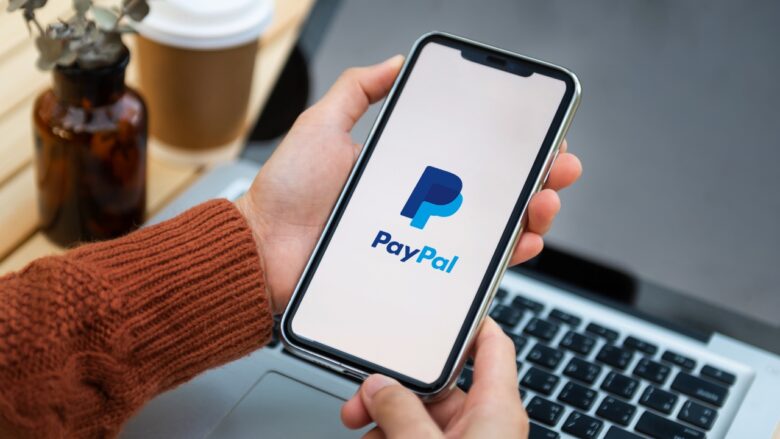 PayPal app open on a phone beside a laptop and coffee