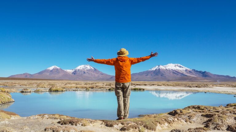 Traveler facing a blue lagoon and snow-capped mountains in South America
