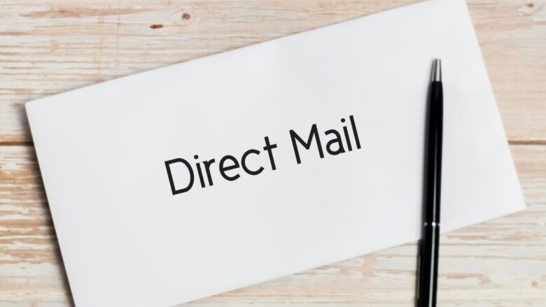 White envelope labeled Direct Mail sits beside a black pen on a wooden desk