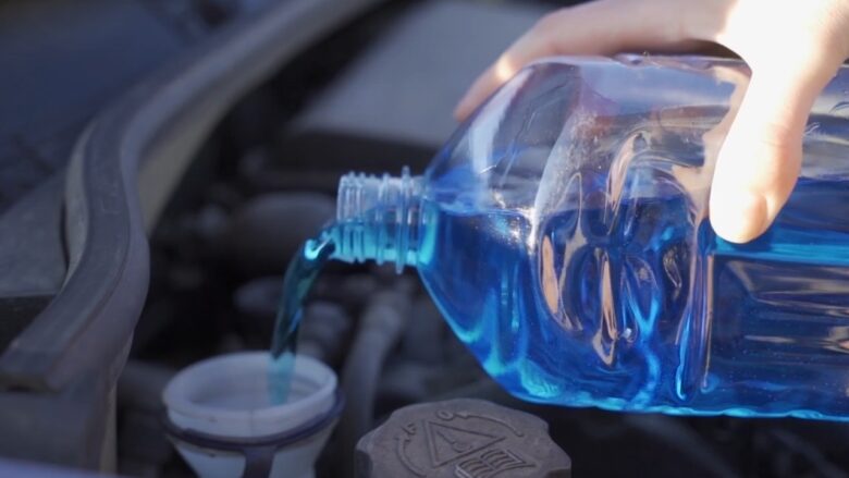Blue washer fluid is added to a car reservoir under the hood