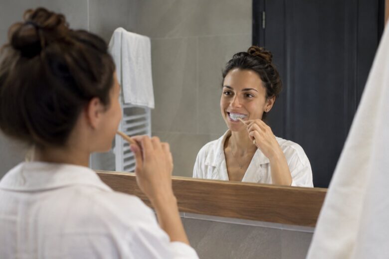 Woman brushing her teeth while looking in the bathroom mirror.