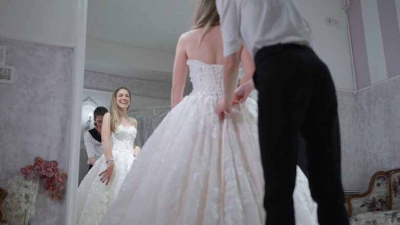 Bride tries on a white gown as a consultant adjusts the skirt