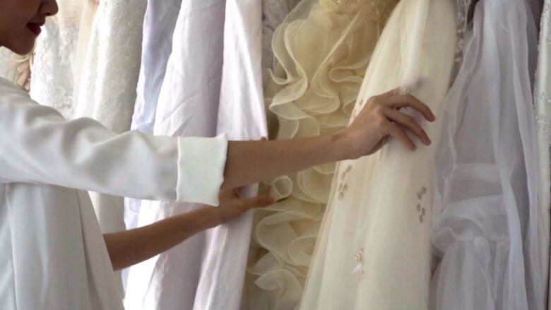 Bride examines white wedding dresses on a boutique rack