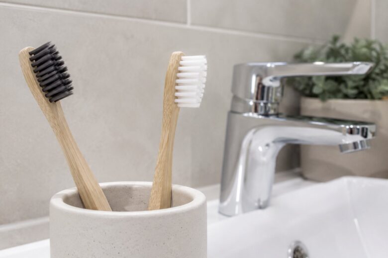 Two bamboo toothbrushes in a ceramic holder beside a sink.