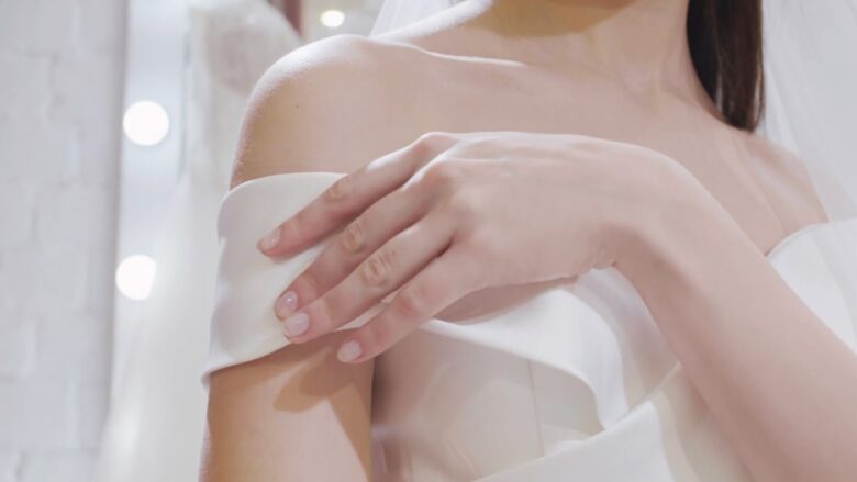 Bride adjusts the off-the-shoulder neckline of a white bridal gown