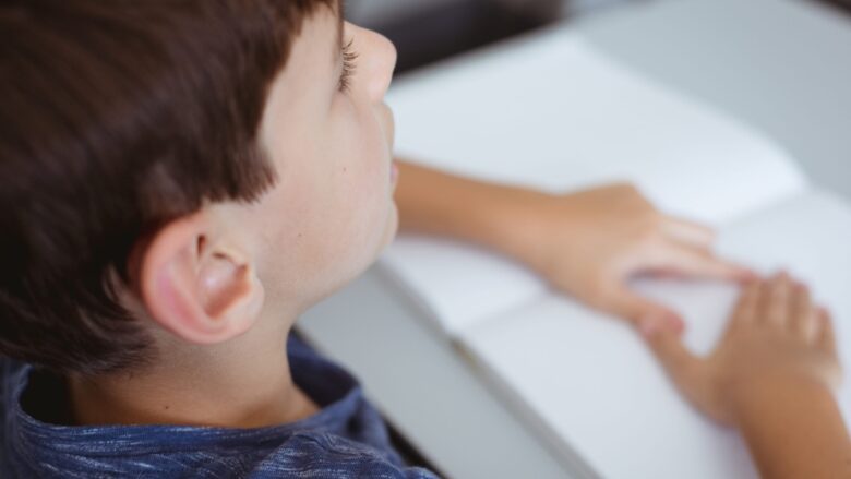 A young boy sits at a desk and listens to someone nearby.