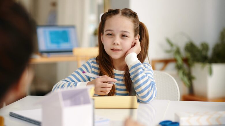 Schoolgirl at a desk with her hand near her ear as she looks at her teacher.