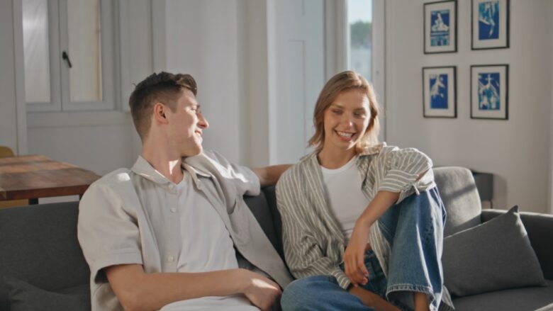 A couple talks and laughs together on a sofa at home.