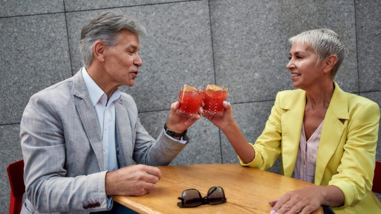 An older man and woman share drinks at a table.