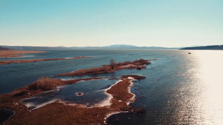 Aerial view of Buško Lake with small islands, calm blue water and distant mountains.