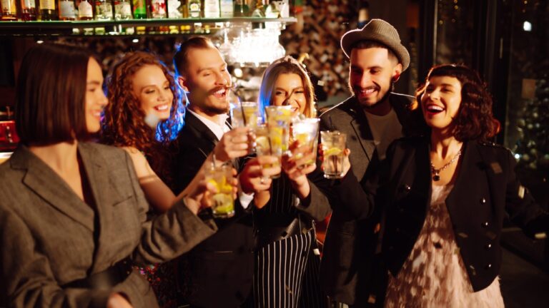 Friends raise cocktails together at a lively bar at night.
