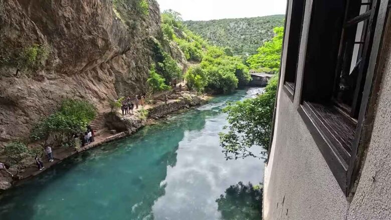 Clear turquoise river beside a rocky cliff and a traditional building in Blagaj.