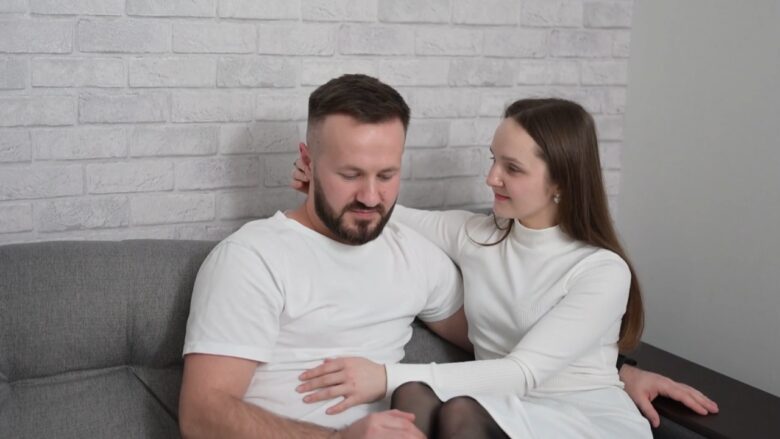 A woman comforts her partner as they sit together on a sofa.