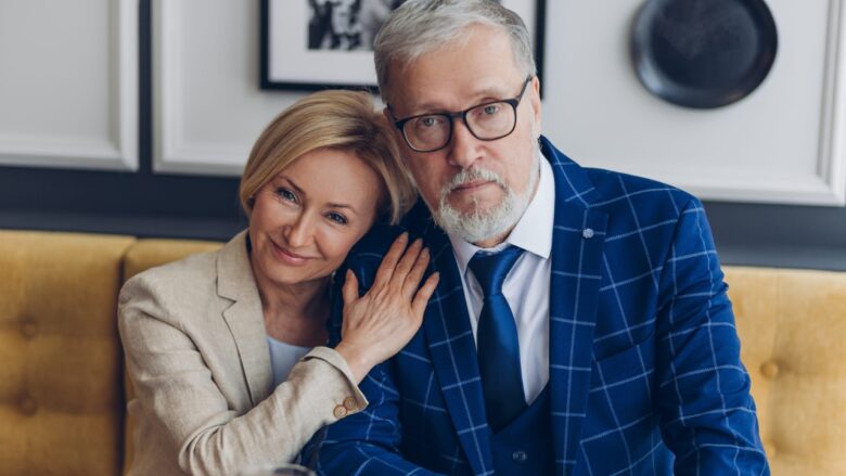 An older couple sits close together on a sofa.