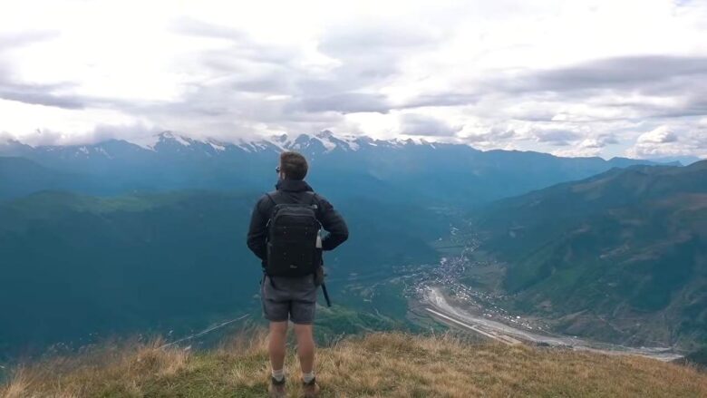 Hiker standing above a wide mountain valley surrounded by high peaks in Georgia.