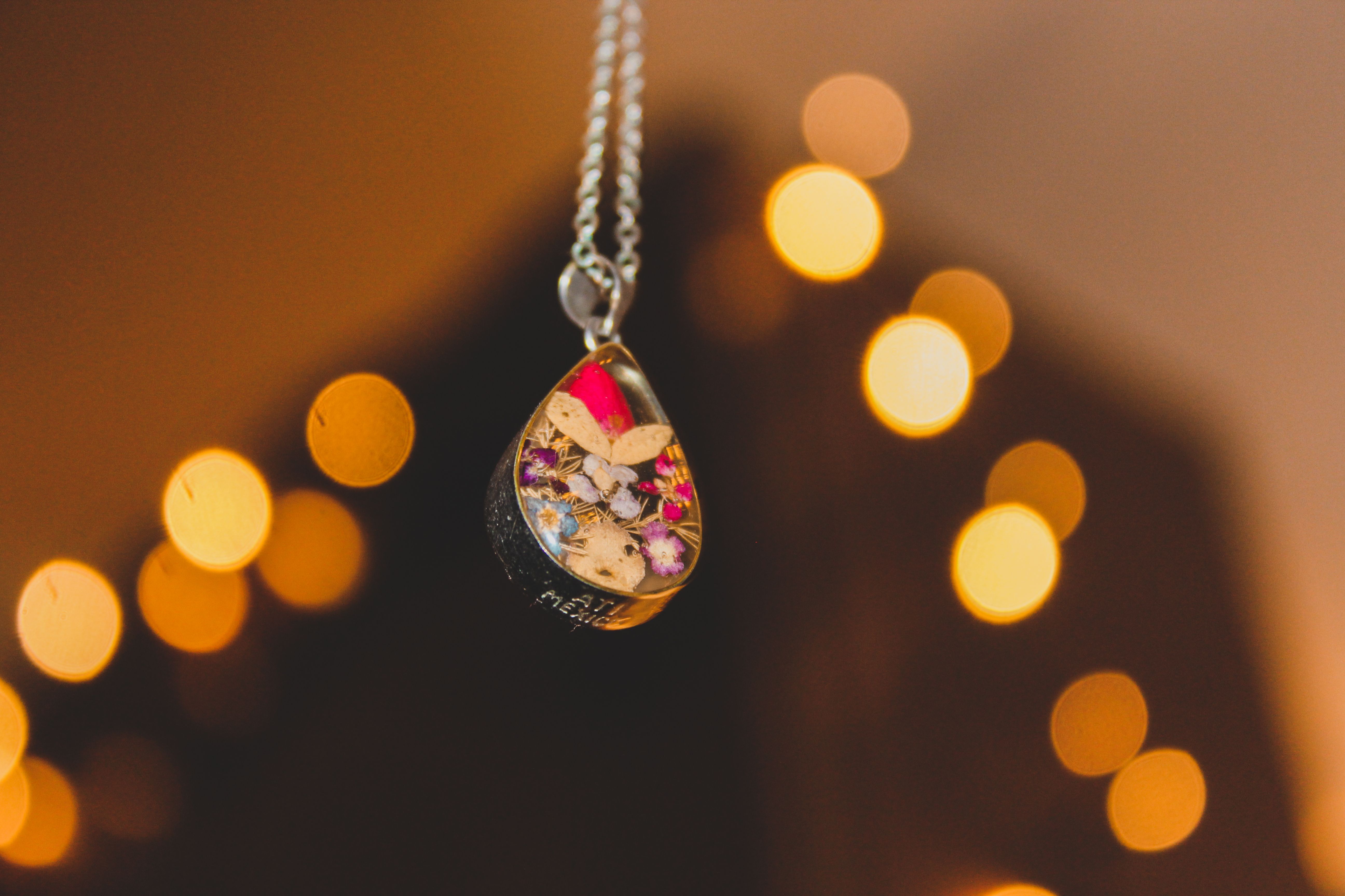 Handmade floral pendant necklace photographed close-up against a warm background.