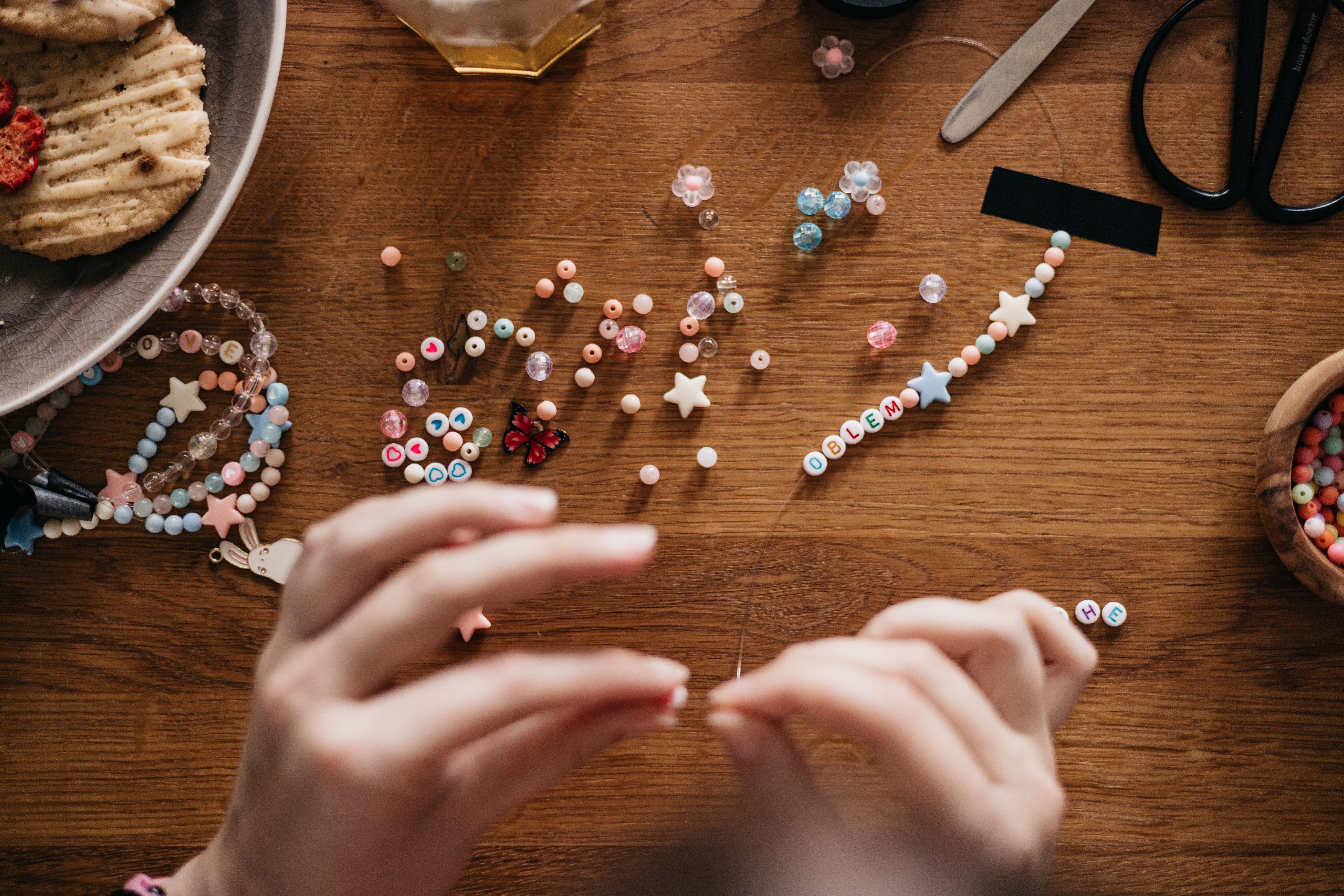Hands assembling personalized beaded jewelry at an organized wooden worktable.